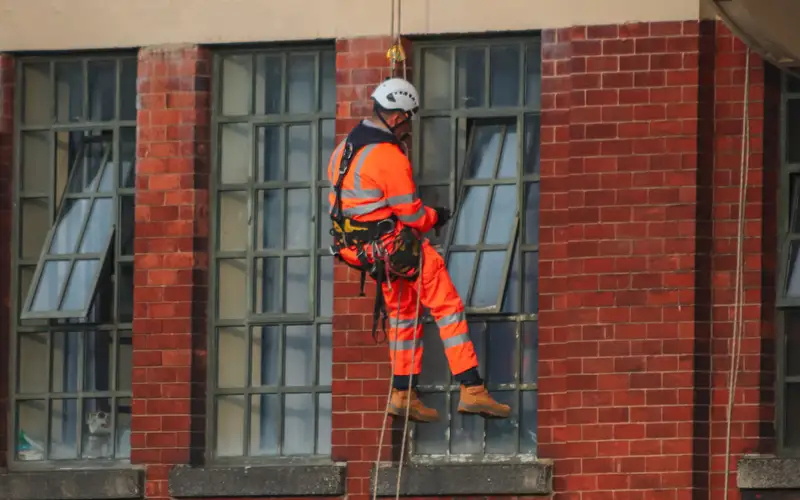 Técnico de trabajos verticales descolgado por cuerdas frente a la fachada de ladrillo de un edificio