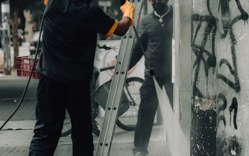 Operarios limpiando pintadas en un muro de la calle
