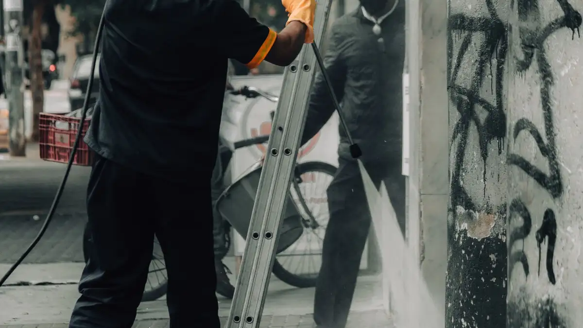 Operarios limpiando pintadas en un muro de la calle