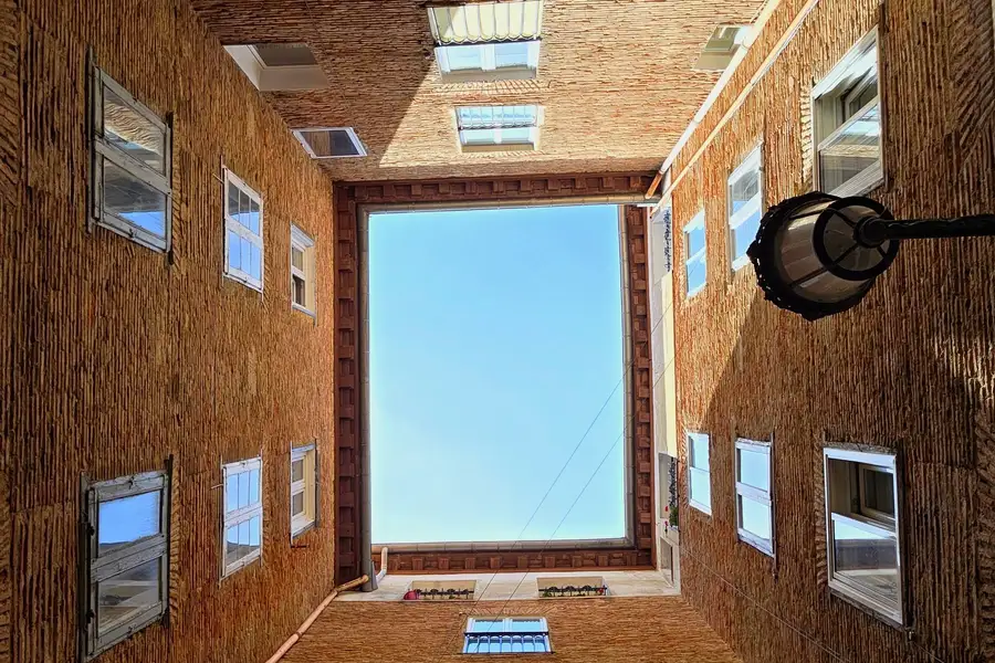 Patio interior de un edificio de ladrillo visto desde abajo, con ventanas en todos los paños