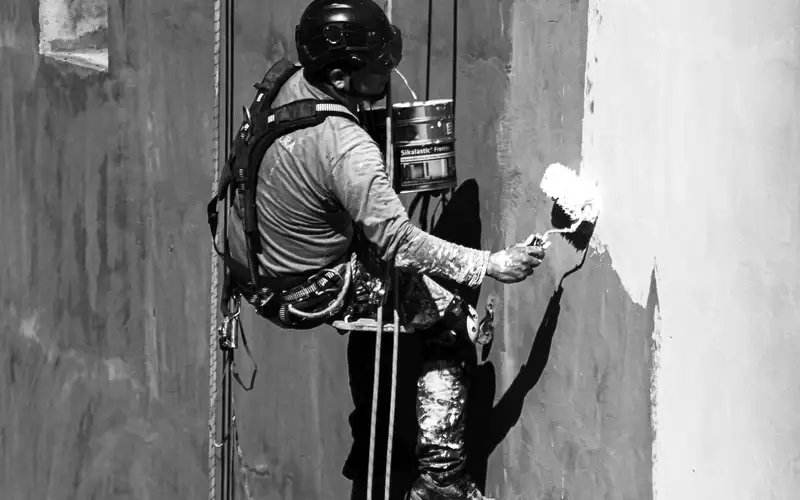 Técnico de trabajos verticales pintando una fachada suspendido con cuerdas