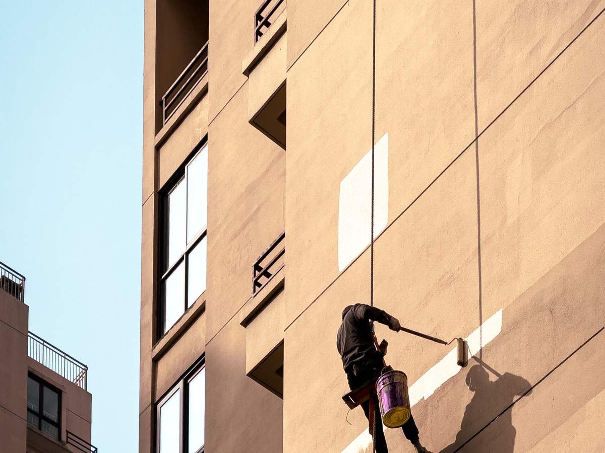 Técnico pintando la fachada de un edificio suspendido de una cuerda