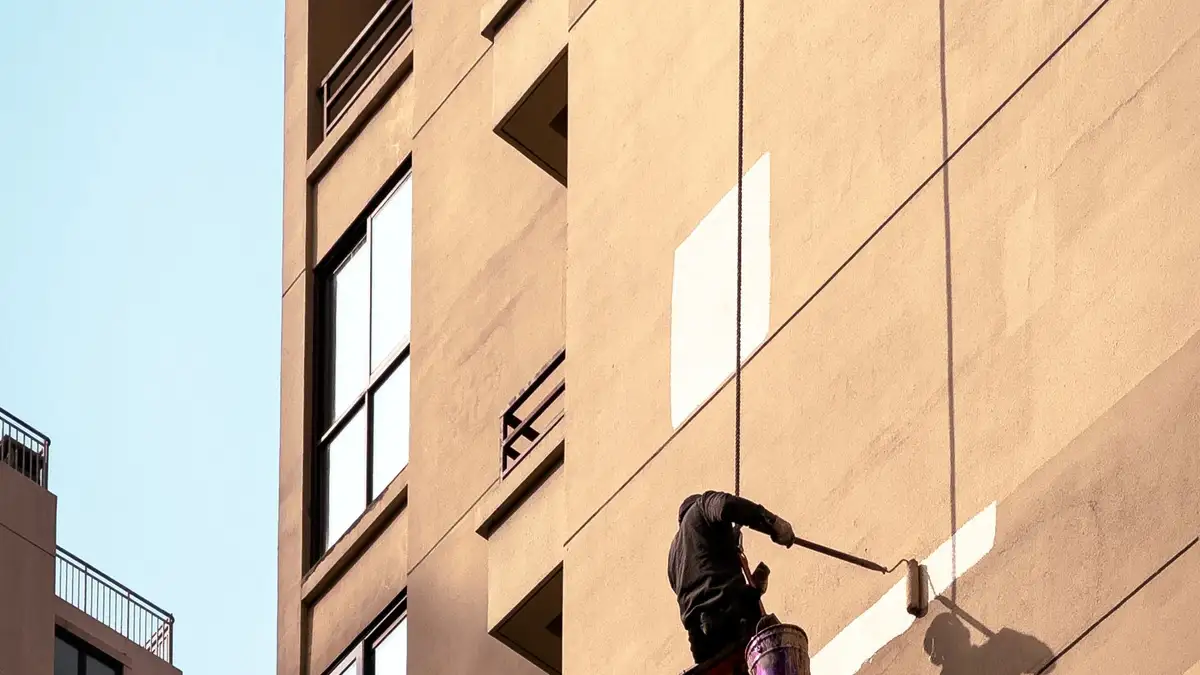 Técnico suspendido con cuerdas pintando la fachada de un edificio